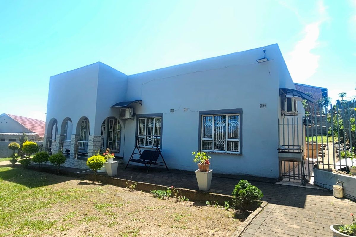 Rear exterior view of the house featuring a paved patio area, security bars on windows, and an installed air conditioning unit.