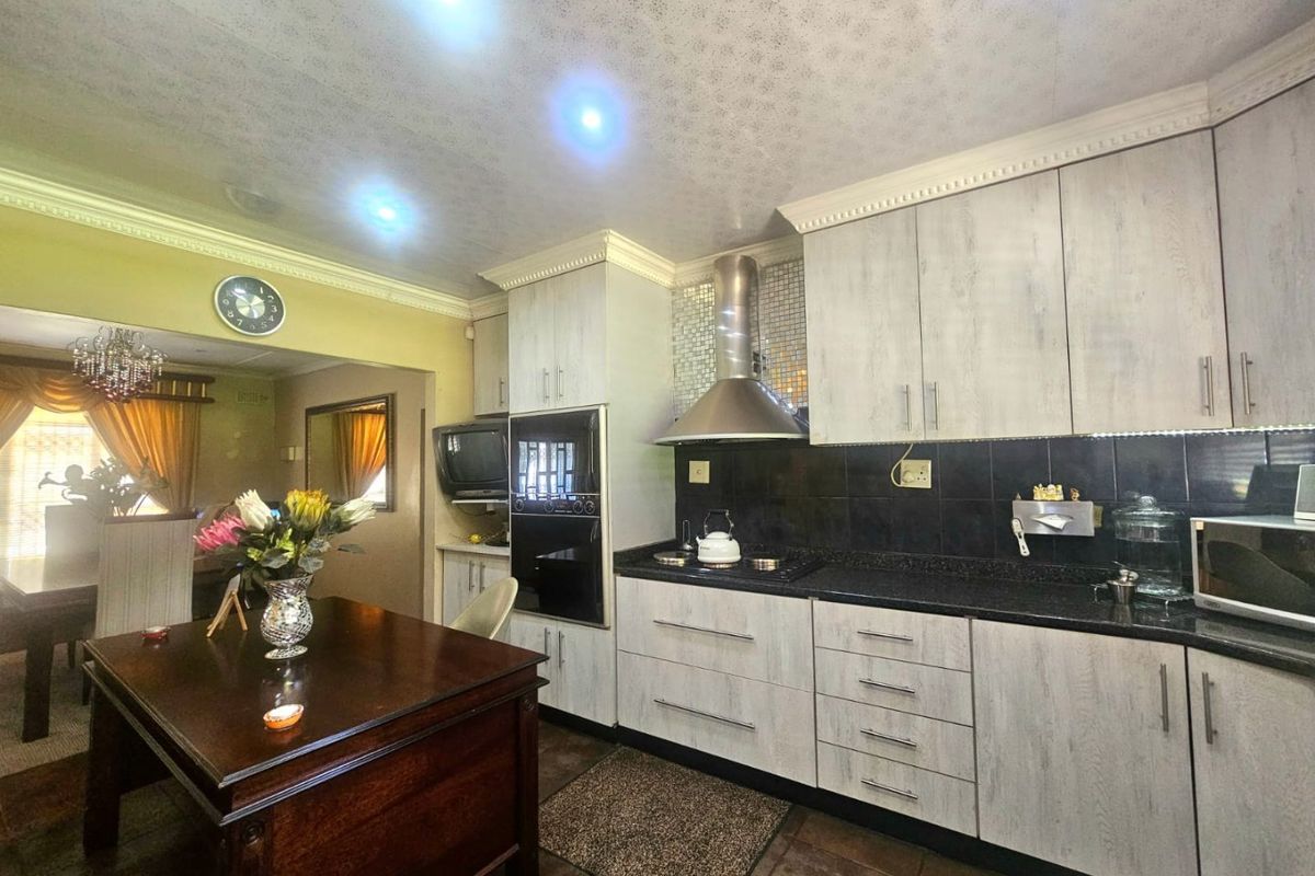 A functional kitchen featuring light-toned cabinetry, granite countertops, a built-in oven, and a stainless steel extractor fan, with an adjacent dining area.
