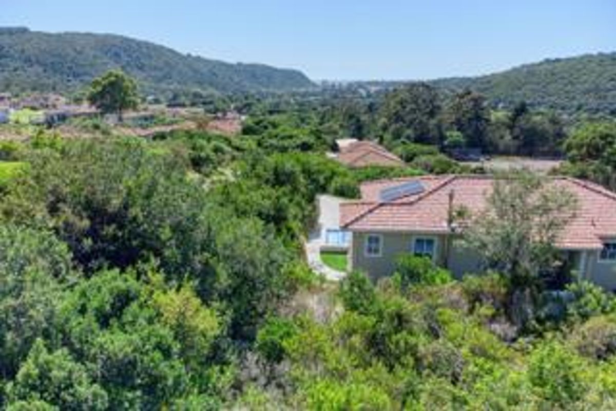 Aerial view of the property featuring a tiled roof with solar panels, a swimming pool, and surrounding lush landscape.