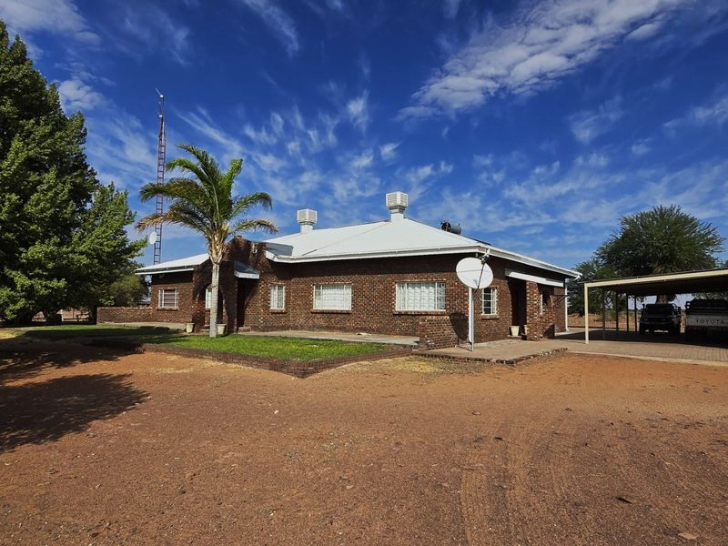A traditional face brick farmhouse featuring a corrugated metal roof, evaporative cooling units, and an attached carport on a spacious rural property.