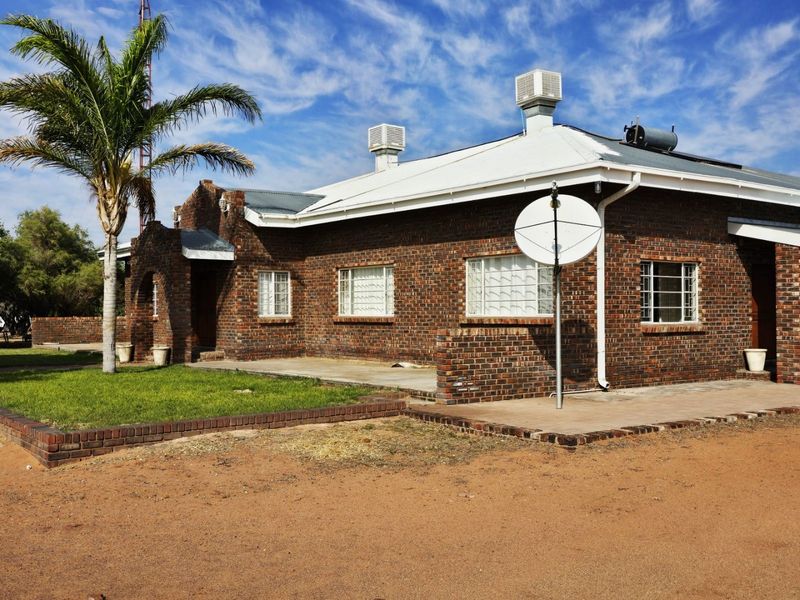 A classic face brick farmhouse exterior featuring a metal roof, solar water heating, evaporative cooling units, and a surrounding concrete patio area.