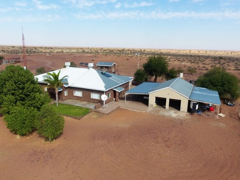 Aerial view of a farmstead featuring a brick main house with a metal roof, solar water heating, and an attached garage and carport structure.