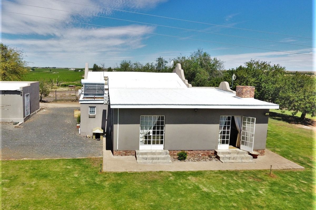 Aerial view of the rear elevation featuring a white corrugated roof, solar water heating system, brick chimney, and a paved patio area.