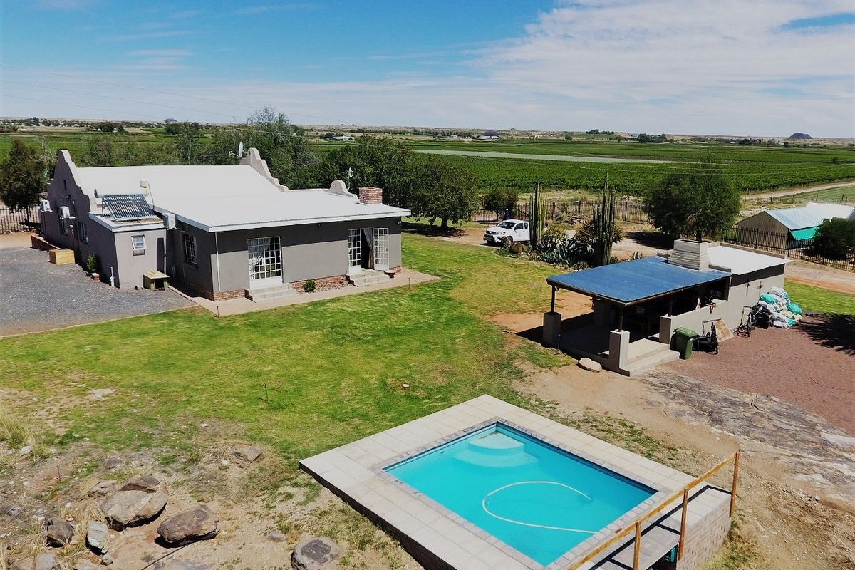 Aerial view of a farm property featuring a main residence with solar heating, a swimming pool, and a separate covered outdoor entertainment area.