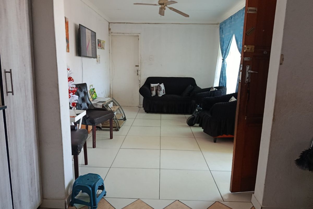 A living room area featuring tiled flooring and a ceiling fan, offering a functional space with potential for cosmetic updates.