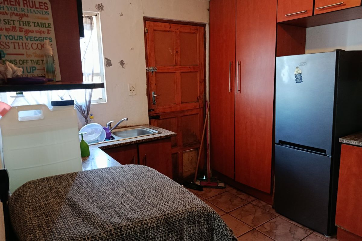 A dated kitchen featuring wood-finish cabinetry, tiled floors, and a stainless steel sink, requiring cosmetic updates to the walls and finishes.