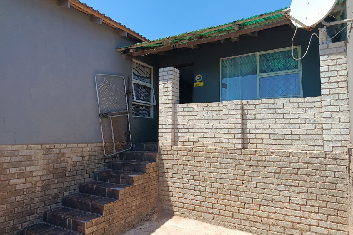 Rear exterior view showing a brick retaining wall, tiled staircase, and basic building structure with security features.