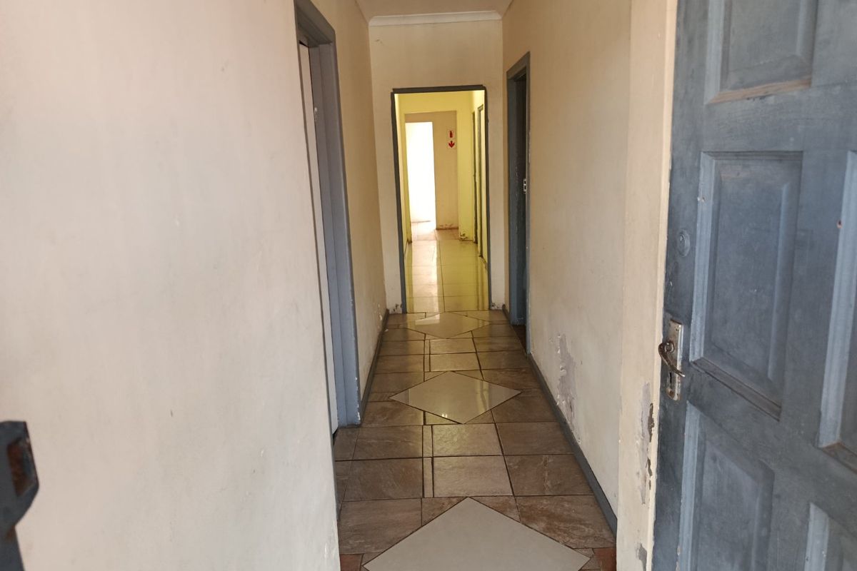 A vacant interior hallway featuring tiled flooring and multiple internal doorways, showing signs of wear on the wall surfaces.
