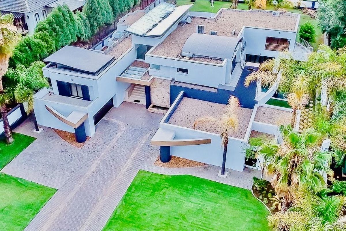 Aerial view of a modern multi-level residential property featuring a paved driveway, landscaped gardens, and contemporary architectural design with flat roof sections.