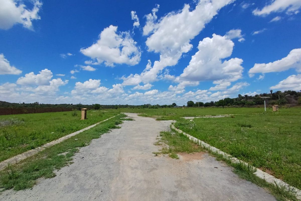 A view of a paved access road within a residential land development, featuring concrete curbing and surrounding open grass plots under a clear sky.