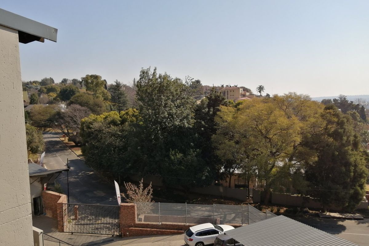 Elevated view overlooking the complex entrance, featuring a carport, perimeter fencing, and established trees in the surrounding neighbourhood.