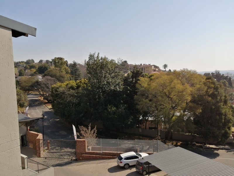 Elevated view overlooking the complex entrance, featuring a carport, perimeter fencing, and established trees in the surrounding neighbourhood.