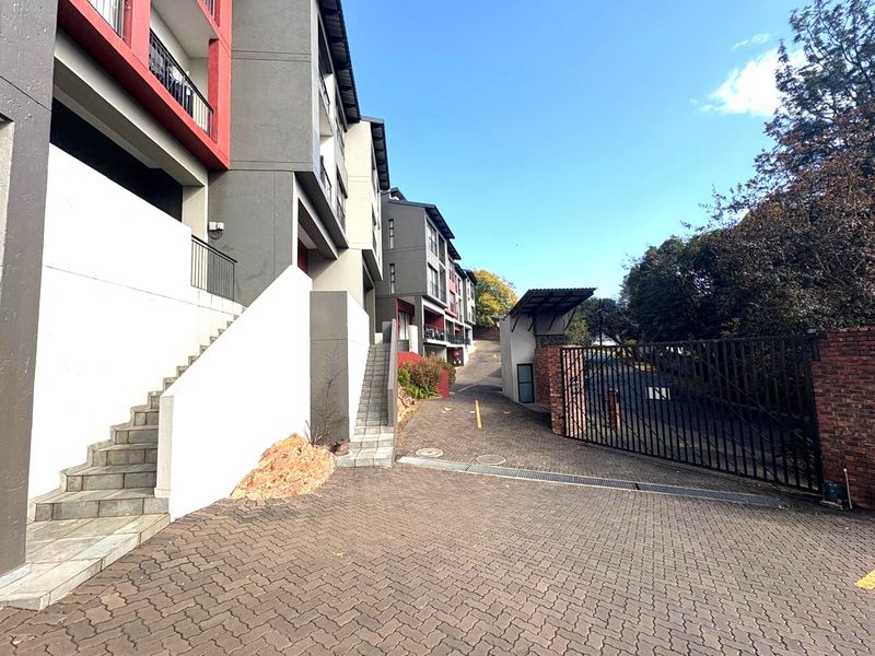 Exterior view of the apartment complex entrance featuring a paved driveway, security gate, and concrete staircases leading to the building units.