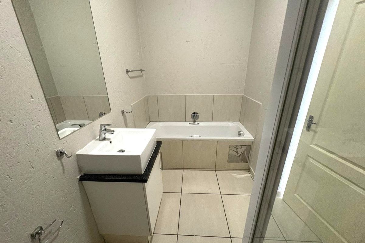 A functional bathroom featuring a bathtub, vanity basin, and tiled finishes, presenting a clean and neutral space ready for minor cosmetic updates.