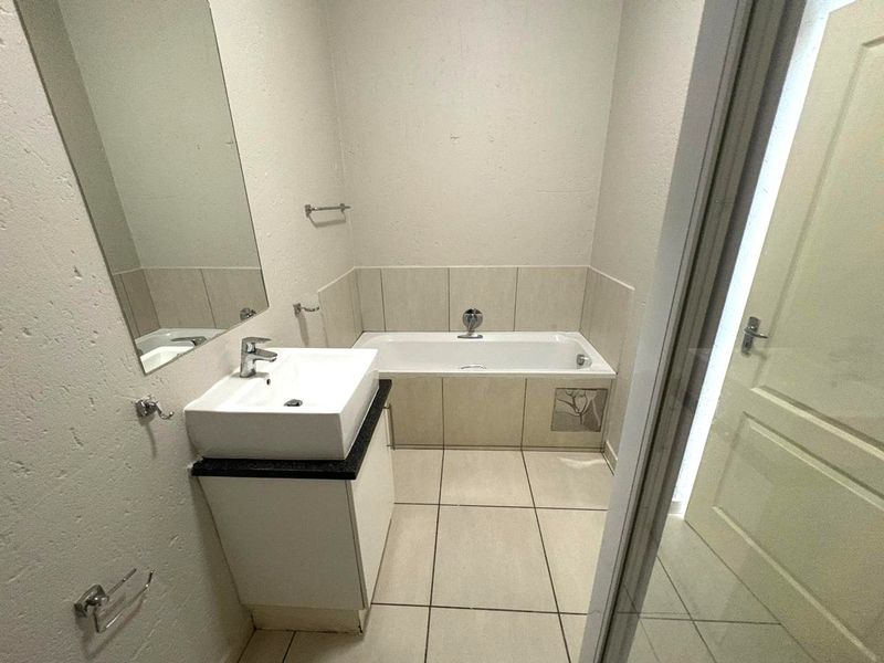 A functional bathroom featuring a bathtub, vanity basin, and tiled finishes, presenting a clean and neutral space ready for minor cosmetic updates.