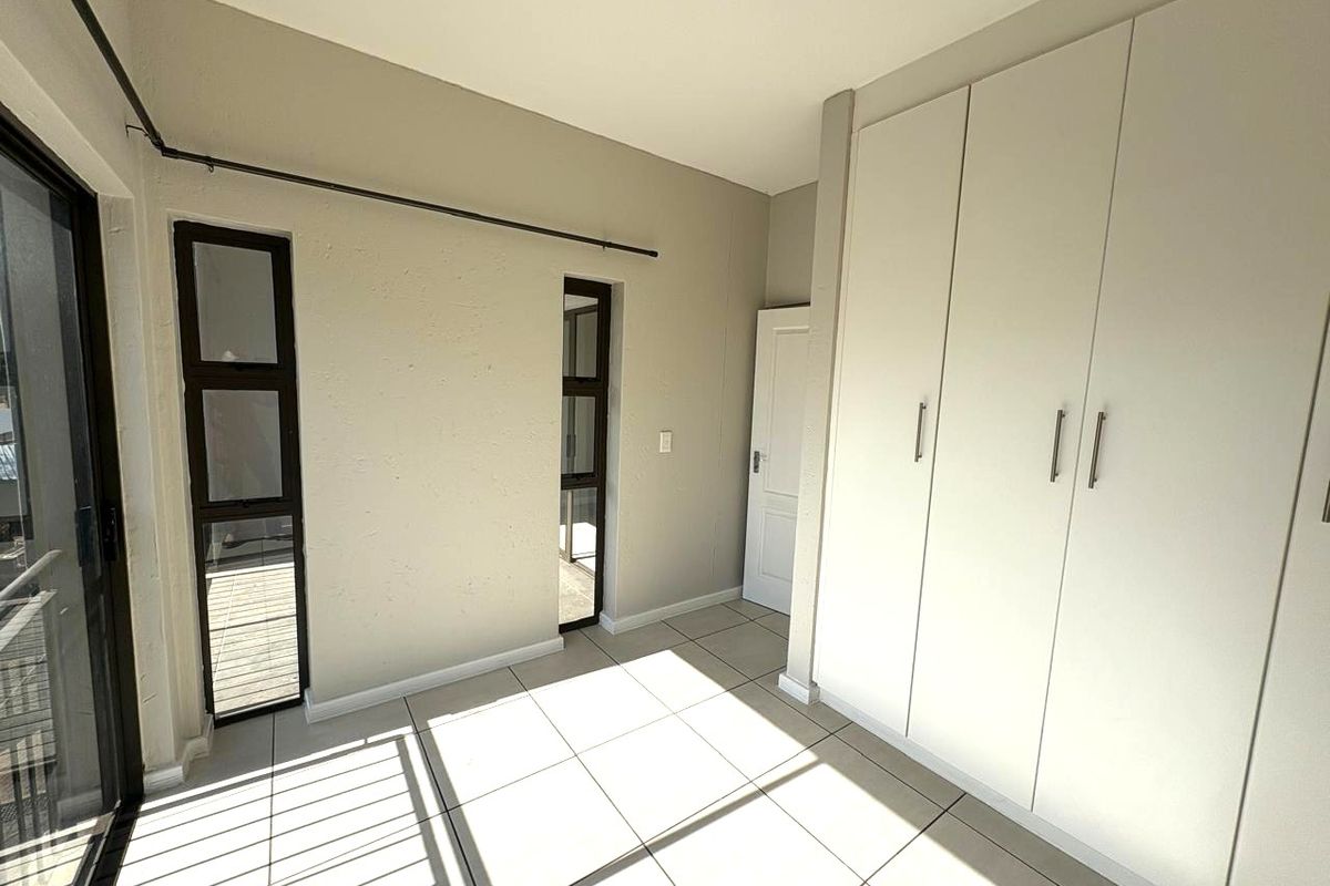 A bright, empty bedroom featuring neutral tiled flooring, built-in cupboards, and access to an outdoor area through a sliding glass door.