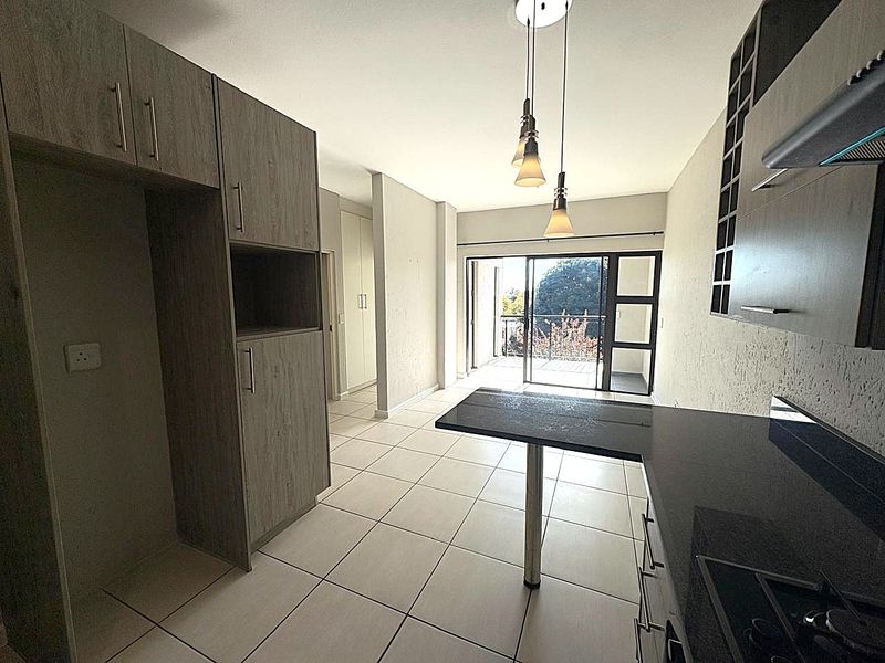 Modern open-plan kitchen and living area featuring sleek cabinetry, stone countertops, tiled floors, and direct access to a private balcony.