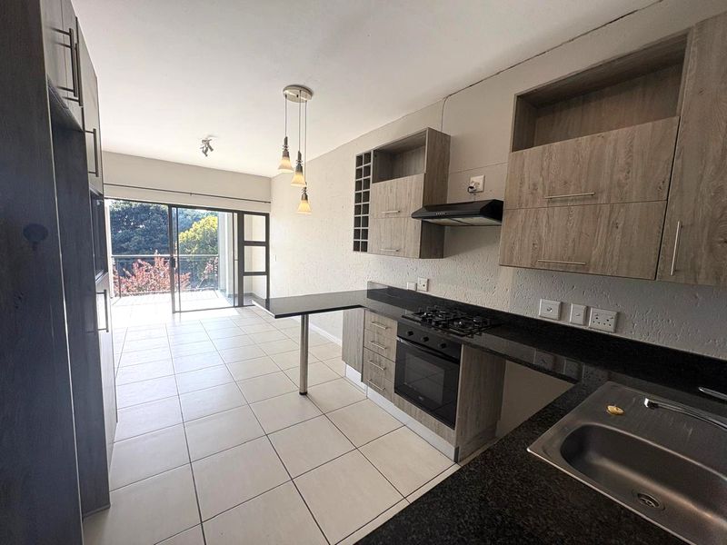 Modern open-plan kitchen featuring granite countertops, built-in oven and hob, and tiled flooring, flowing seamlessly into a bright living area with balcony access.