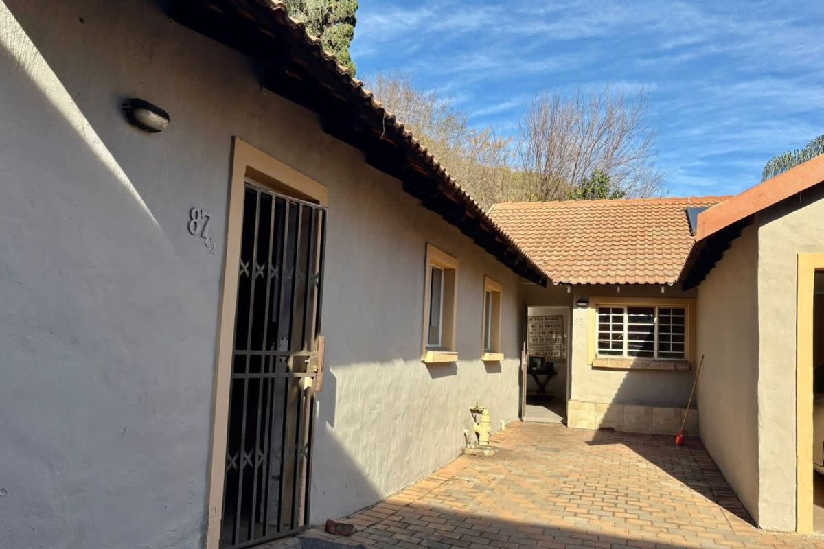 A view of the exterior side entrance and paved courtyard area featuring tiled roofing and security gates.