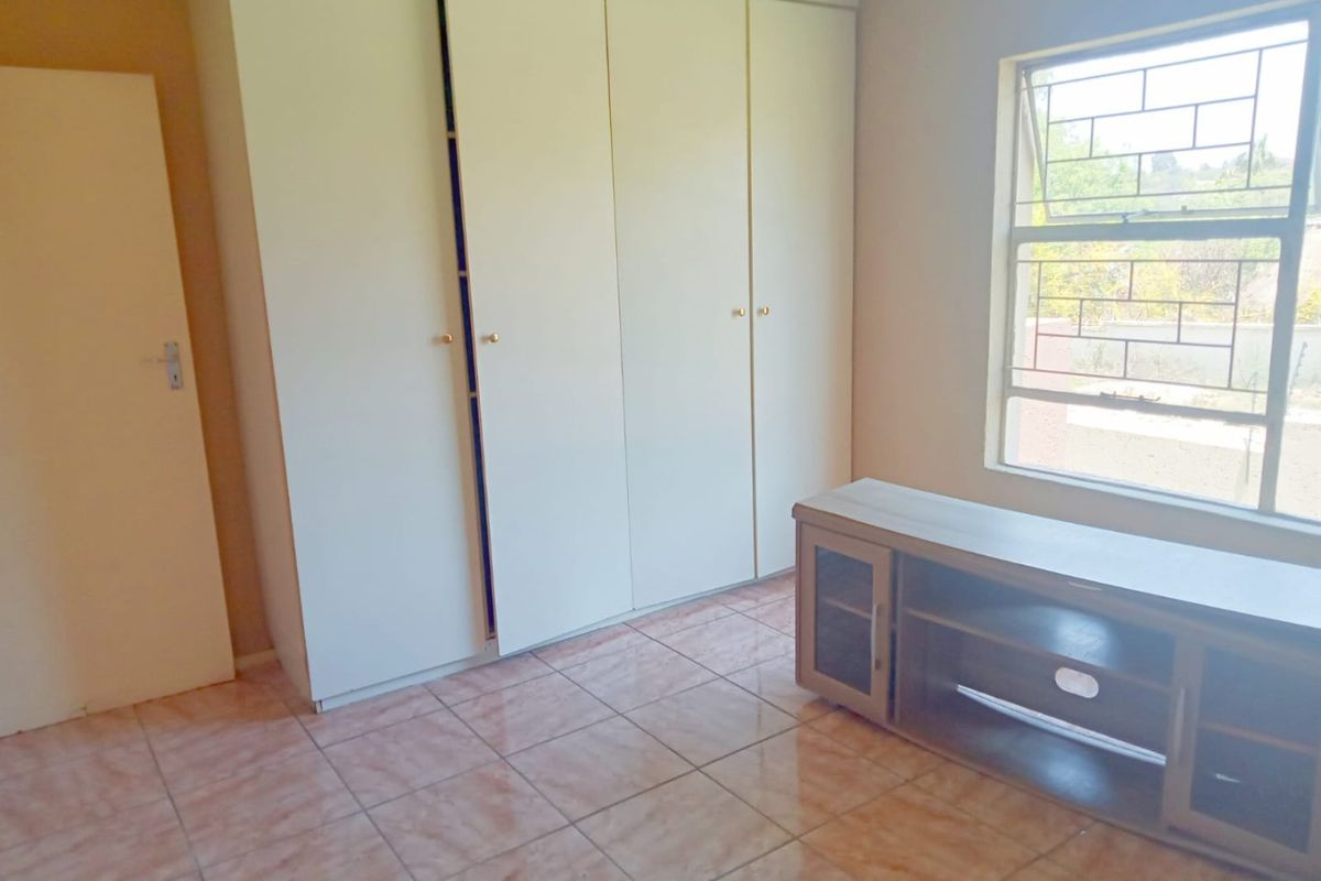 A bedroom featuring built-in wardrobes, tiled flooring, and a window with security bars.