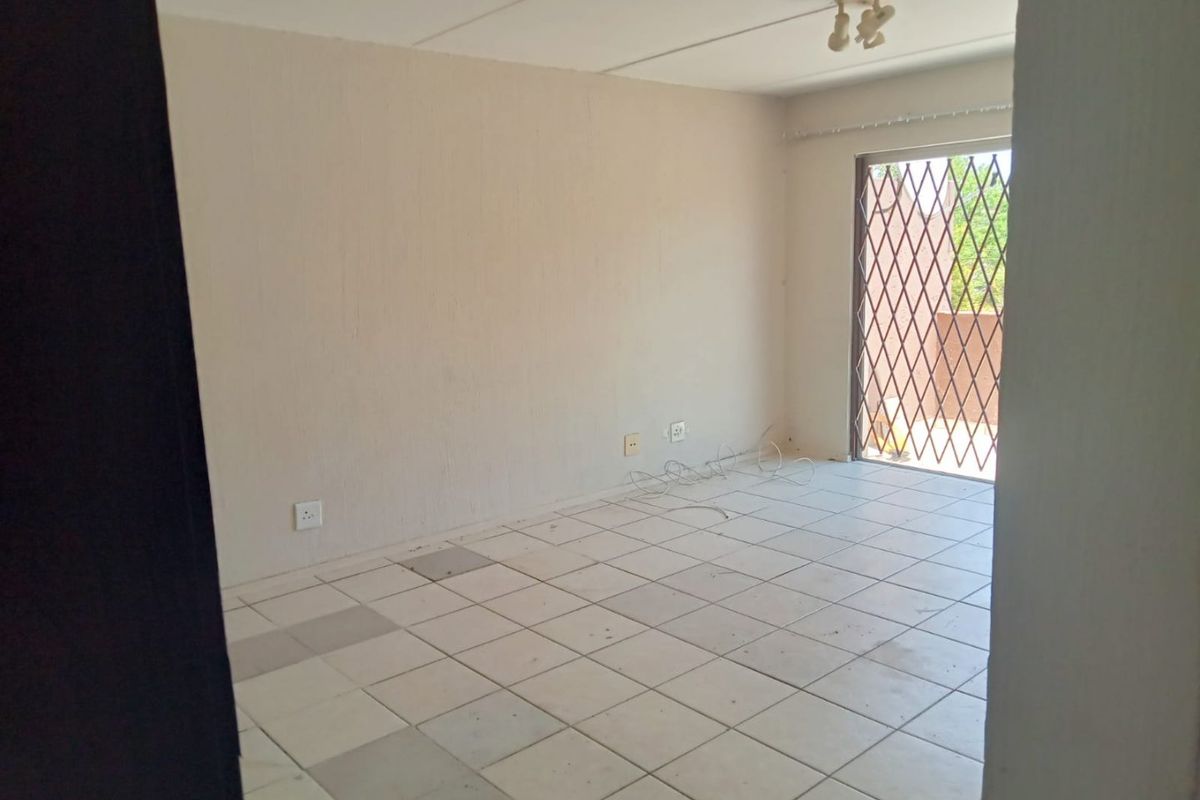 An empty living room featuring tiled flooring, a ceiling light fixture, and a sliding door with a security gate leading to an outdoor area.