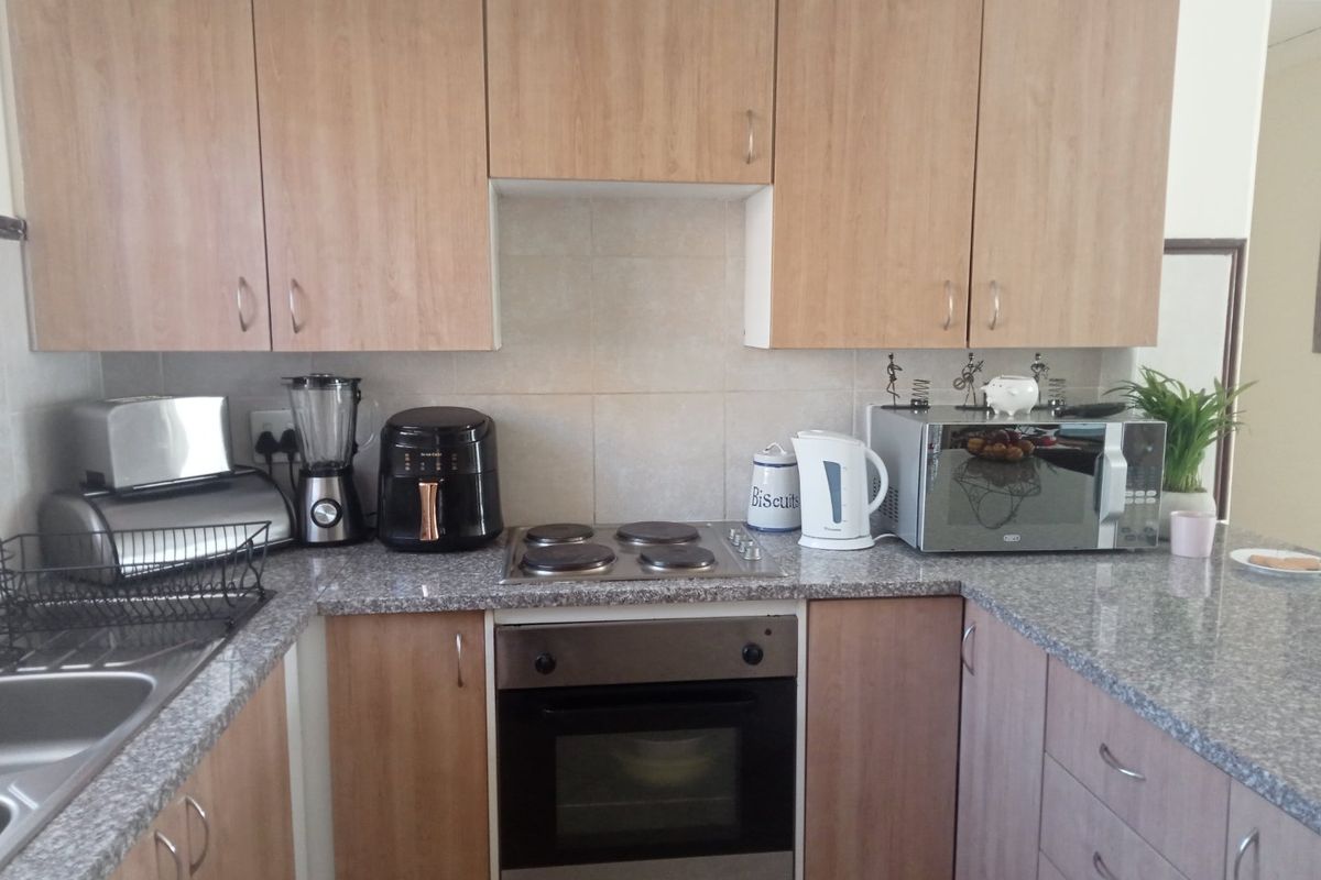 A functional kitchen featuring light wood-finish cabinetry, granite-look countertops, a built-in oven, and a four-plate electric hob.