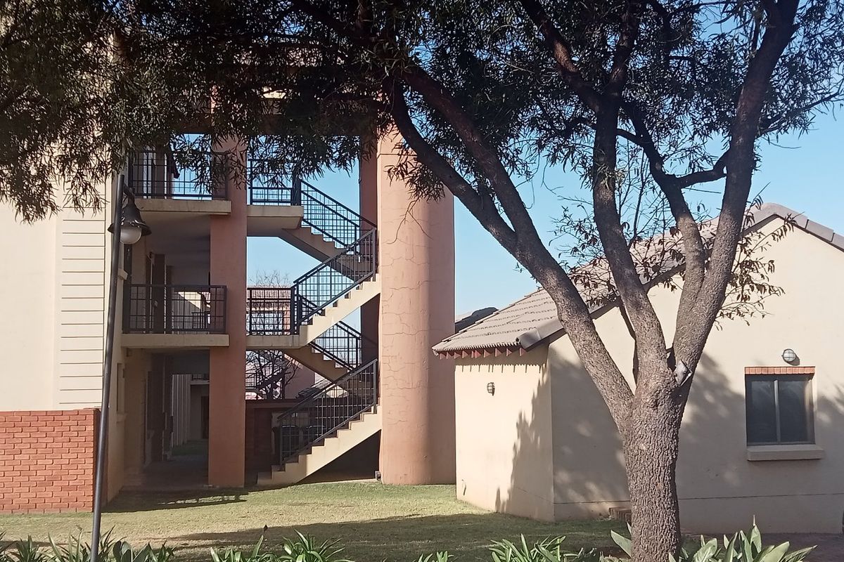Exterior view of an apartment complex featuring a multi-level staircase, tiled roof structure, and landscaped garden area.