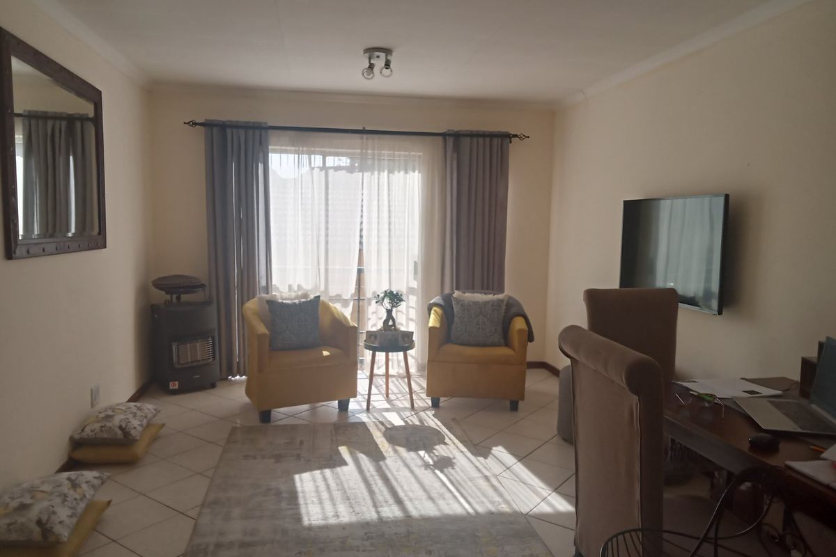 A bright living room featuring tiled flooring, a sliding glass door leading to a balcony, and a wall-mounted television.