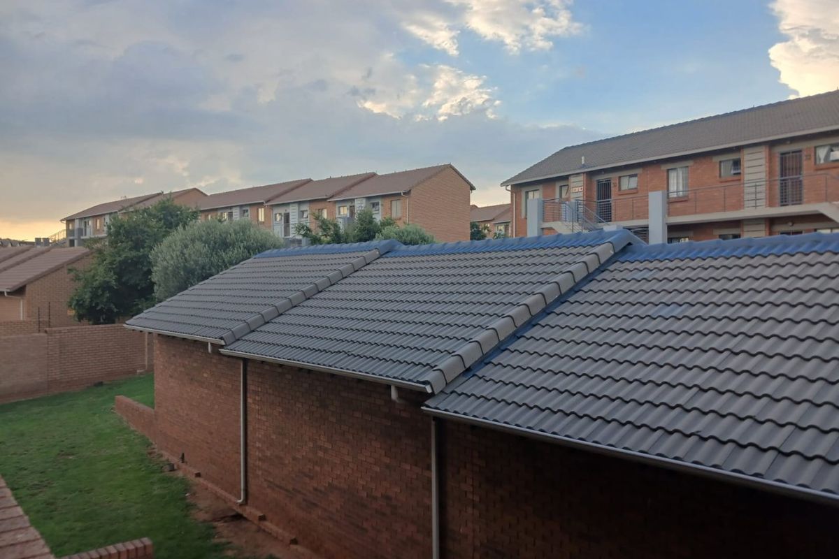 An elevated view of the apartment complex, showcasing the tiled roof structure, brick exterior walls, and surrounding communal garden area.