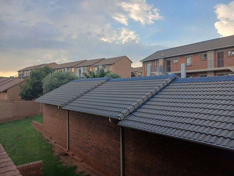 An elevated view of the apartment complex, showcasing the tiled roof structure, brick exterior walls, and surrounding communal garden area.