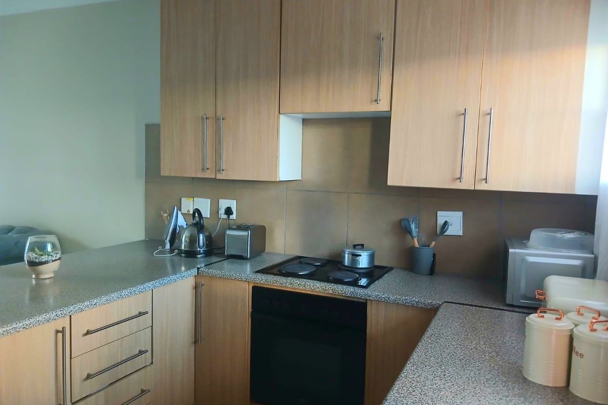 A functional kitchen featuring light wood-finish cabinetry, granite-look countertops, a built-in electric oven, and a glass-ceramic hob with a tiled backsplash.