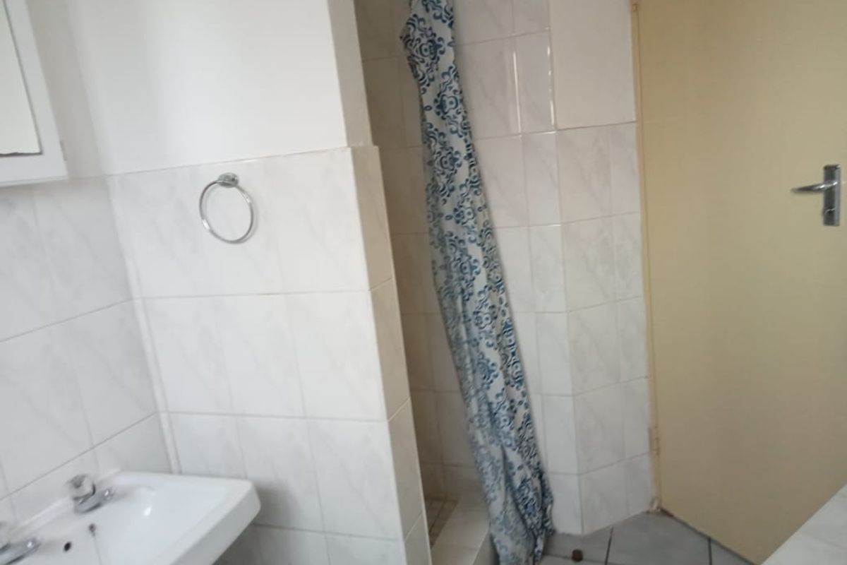 A functional bathroom featuring a tiled shower enclosure, wall-mounted basin, and neutral wall tiles.