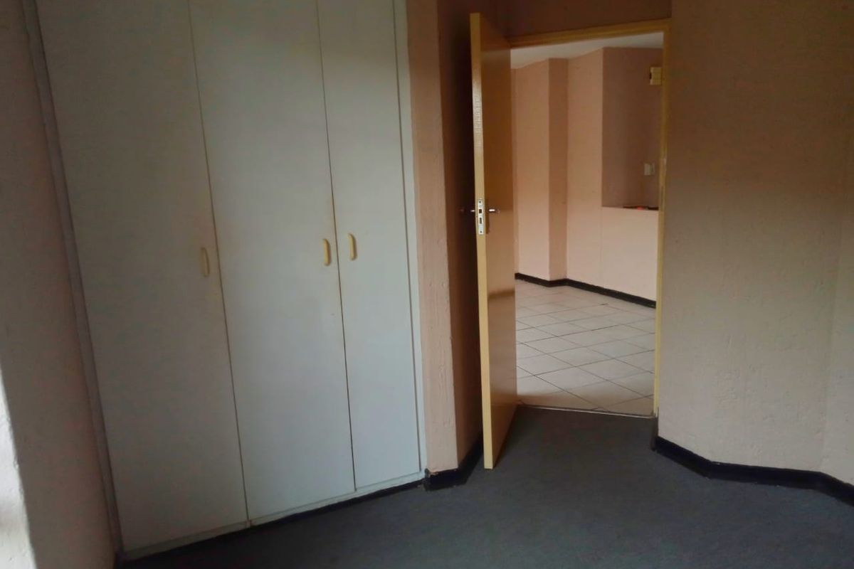 A bedroom featuring built-in cupboards and carpeted flooring, with an open doorway leading to an adjacent tiled living area.