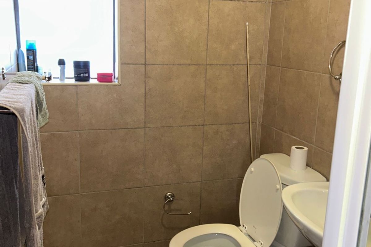 A compact bathroom featuring floor-to-ceiling wall tiles, a standard toilet, and a wall-mounted basin with a window for natural light.