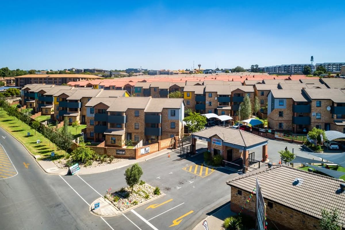 Aerial view of the apartment complex entrance, featuring paved access roads, security gatehouse, and multiple residential blocks with tiled roofs.