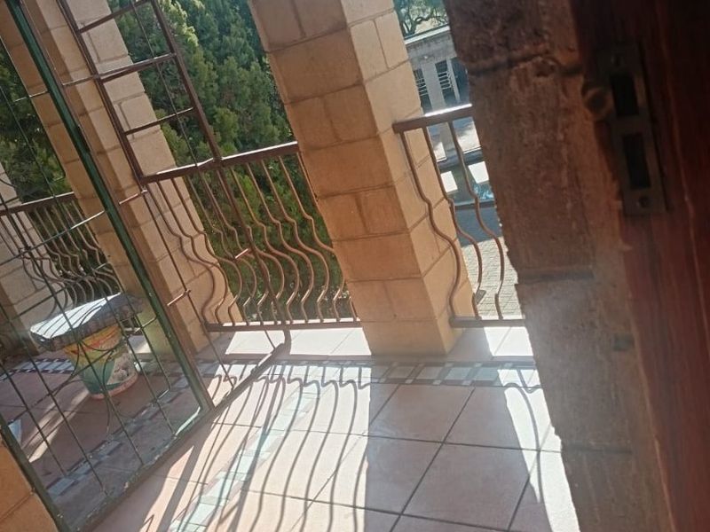 A covered balcony featuring brick pillars, tiled flooring, and metal security screening, offering an outdoor space with potential for enhancement.