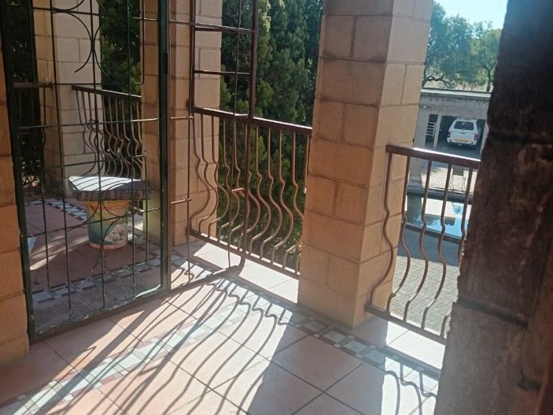 A covered balcony featuring tiled flooring, brick pillars, and wrought iron security features, offering an outdoor space with views of the property grounds.