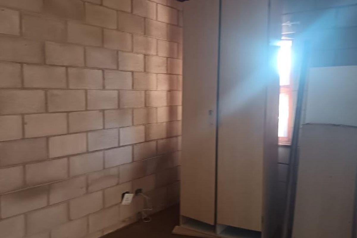 A bedroom featuring exposed blockwork walls, a built-in wardrobe, and carpet flooring, requiring cosmetic updates to improve the overall finish.