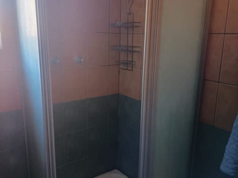 A dated shower cubicle featuring two-tone ceramic wall tiles and a standard shower tray in an apartment bathroom.