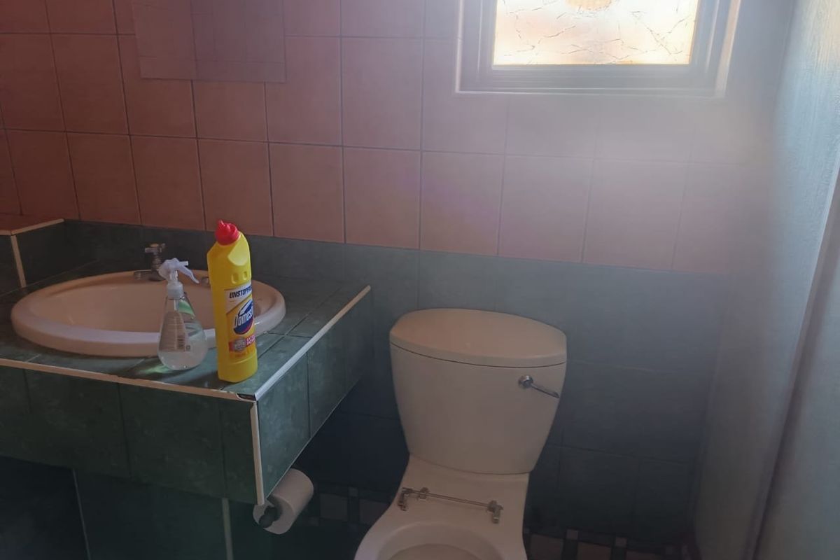 A dated bathroom featuring a tiled vanity with a drop-in basin and a standard toilet. The space requires cosmetic updates and a new toilet seat.