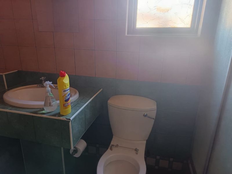 A dated bathroom featuring a tiled vanity with a drop-in basin and a standard toilet. The space requires cosmetic updates and a new toilet seat.