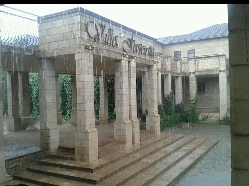 Exterior view of the stone-clad building entrance featuring a covered portico, stone columns, and wide steps, captured during rainy weather.