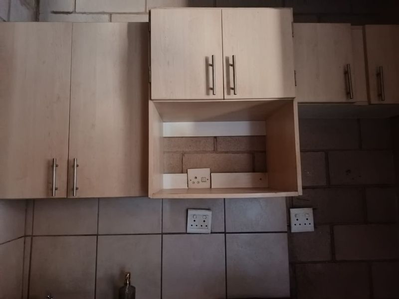 A kitchen area featuring light wood-look cabinetry, tiled backsplash, and exposed brick walls requiring finishing and maintenance.