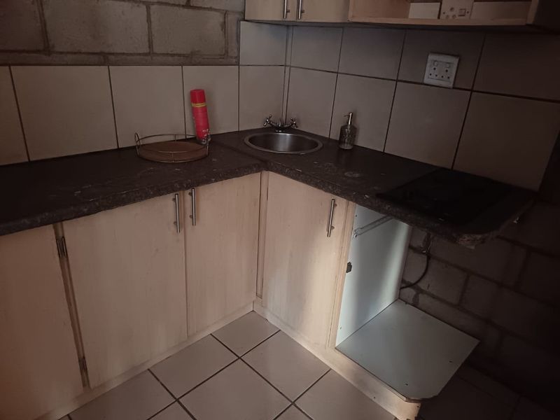 A compact kitchen area featuring laminate countertops, a stainless steel sink, and built-in cabinetry, currently requiring cosmetic updates and finishing to the exposed wall.