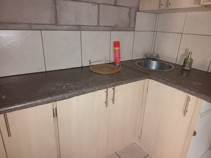 A compact kitchen area featuring laminate cabinetry, a stainless steel sink, and an unfinished concrete block wall section requiring cosmetic attention.
