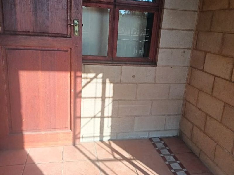 A covered patio area featuring tiled flooring, exposed brick walls, and a timber door with an adjacent window.