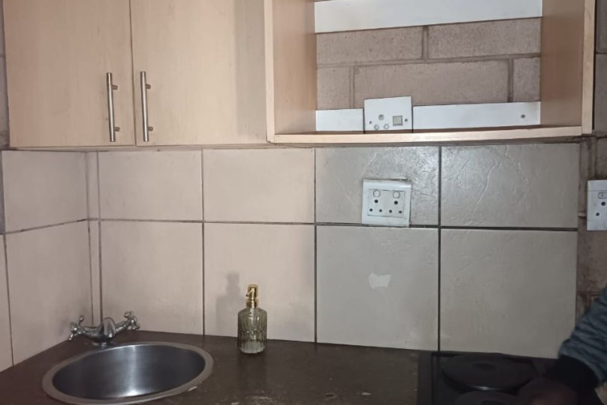 Compact kitchen area featuring laminate cabinetry, a stainless steel sink, and a built-in electric hob with tiled splashback.