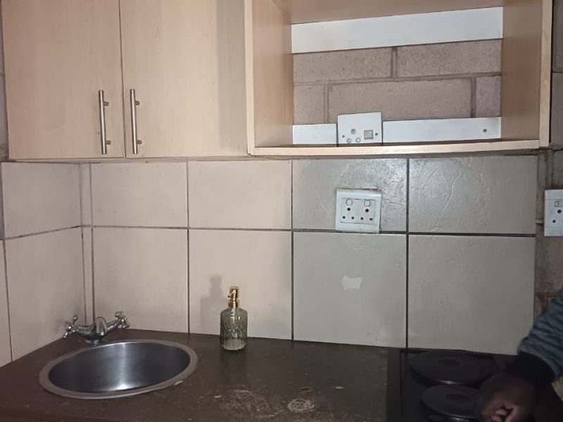 Compact kitchen area featuring laminate cabinetry, a stainless steel sink, and a built-in electric hob with tiled splashback.