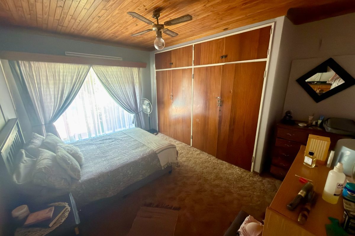 A bedroom featuring built-in wooden cupboards, a timber tongue and groove ceiling, and a ceiling fan, with carpeted flooring throughout.