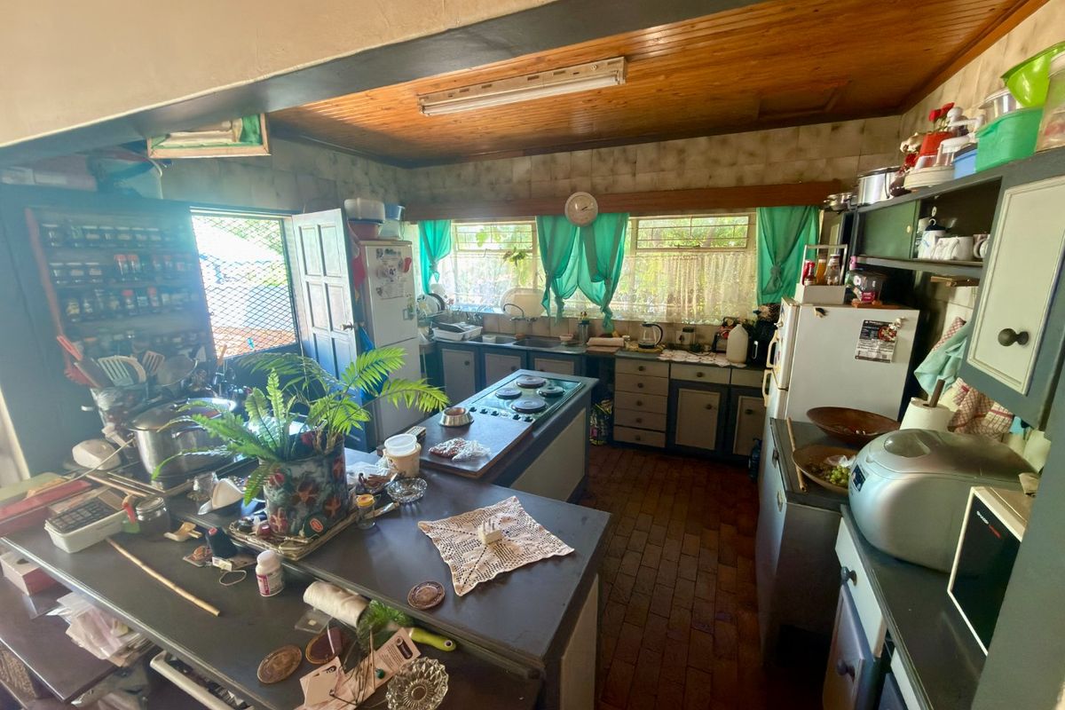 A dated kitchen featuring timber ceilings, brick flooring, built-in cabinetry, and a central island with a cooktop, offering significant potential for modernization.